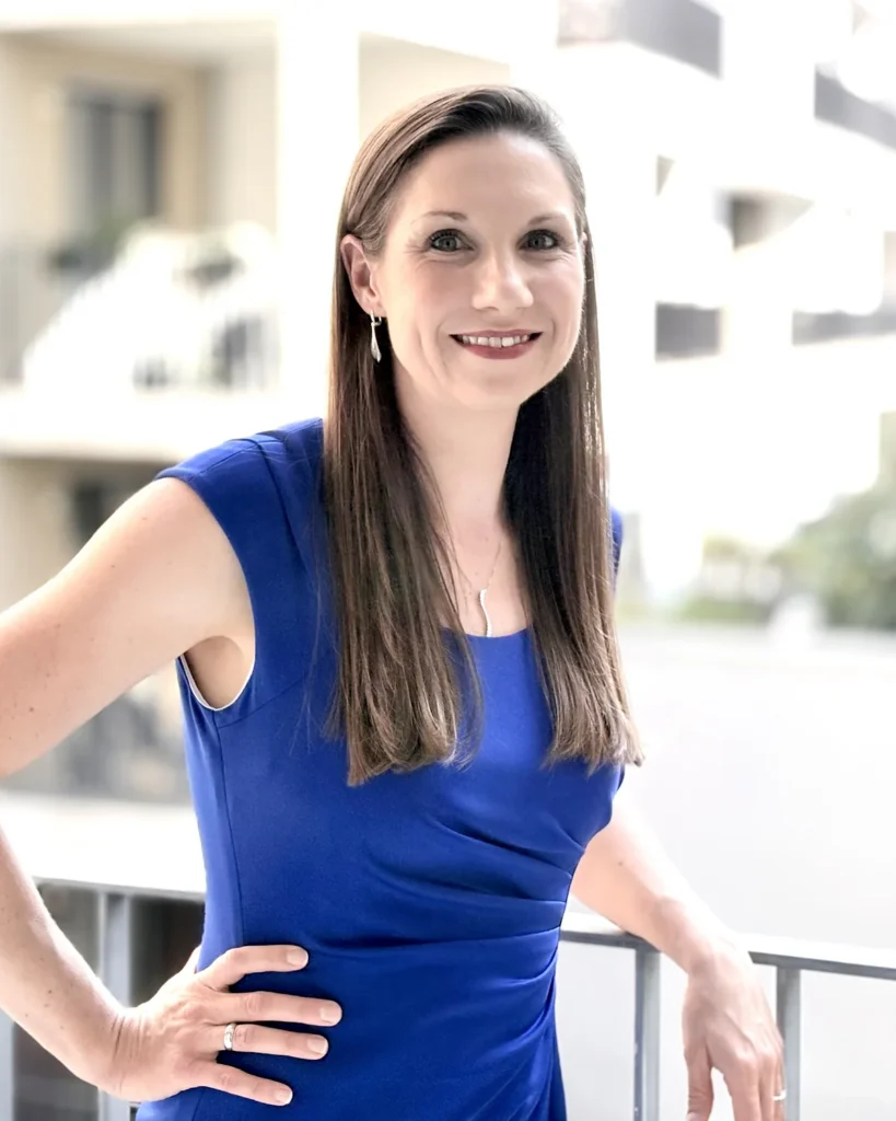 Dawn standing on a sunny balcony in a blue dress, smiling