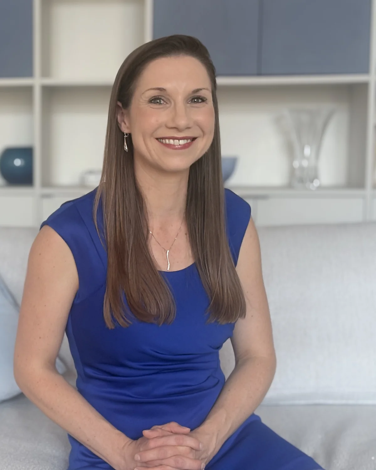 Dawn sitting relaxed on a sofa in a blue dress, smiling